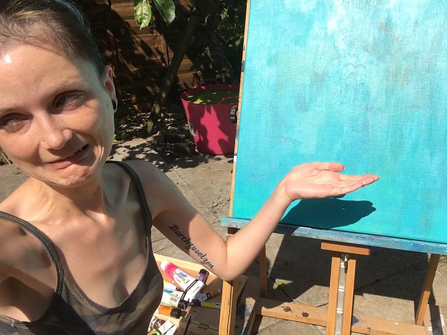 'I've idea what I'm doing' Blog Post Photo of me pulling a face and gesturing at a blue canvas painting.