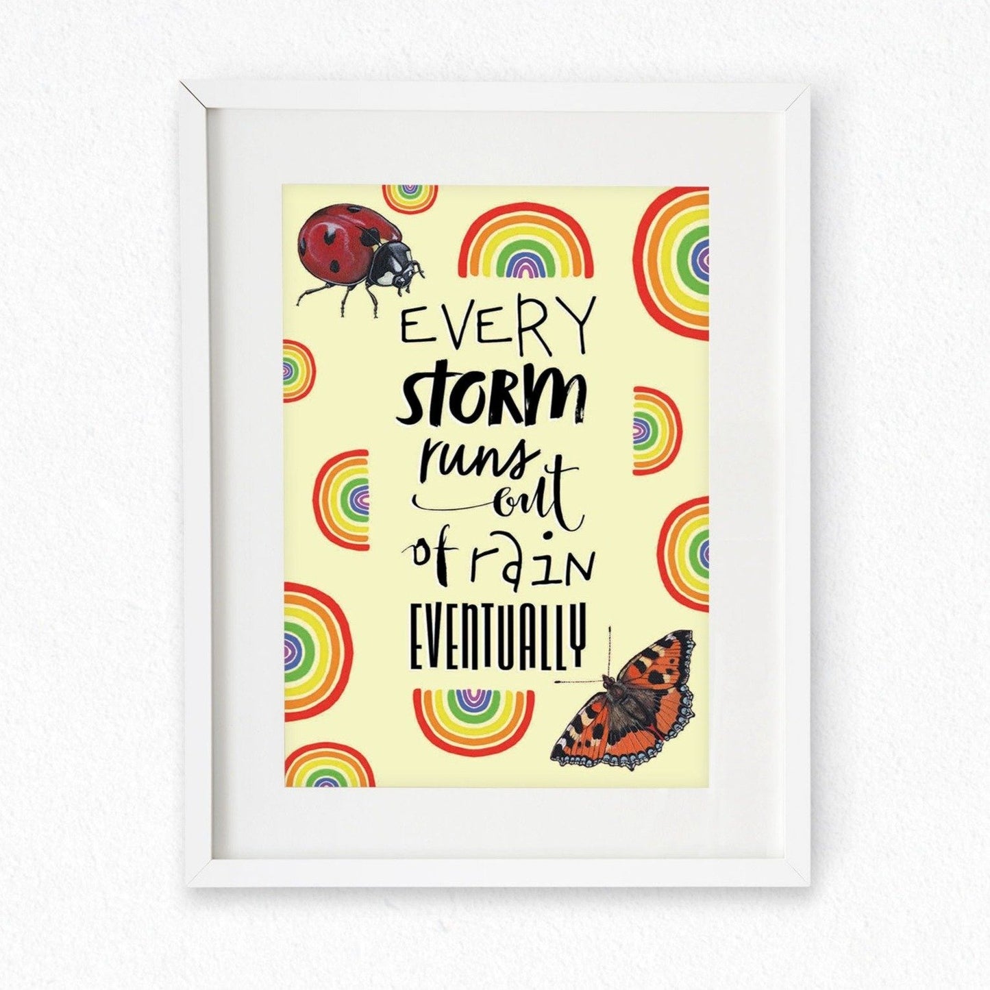Framed mock up of an A4 Print; the design has a yellow background covered in rainbows, a ladybird top left, a butterfly bottom right, and the words 'Every storm runs out of rain eventually' in the centre. Artwork by Jenny Pond, JPArtwork