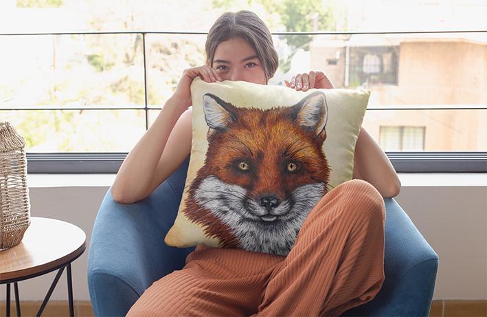 Woman holding a Fox Cushion on her lap, while sitting in an armchair smiling