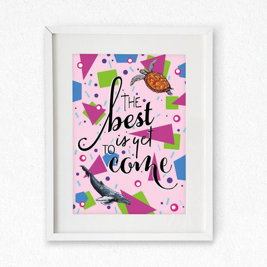 Framed mock up of an A4 Print; the design has a pale pink background covered in shapes: green squares, pink triangles, blue hexagons, pink and white dots, purple dots, and light blue confetti lines. A sea turtle is top right, a blue whale bottom left, and the words 'The best is yet to come' in the centre. Artwork by Jenny Pond, JPArtwork